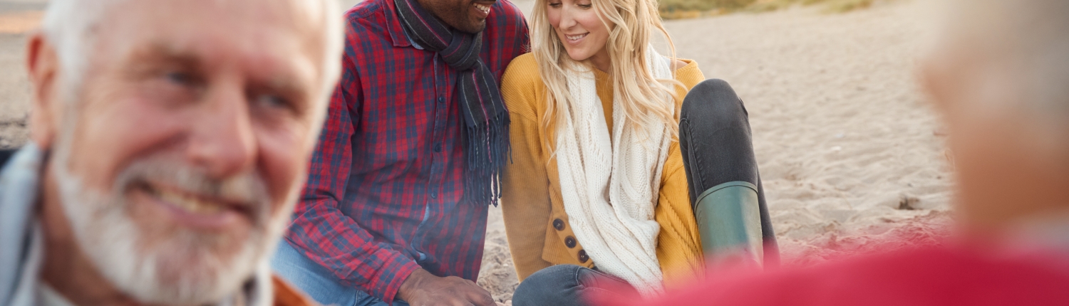 Loving Couple Relaxing By Fire With Senior Parents On Winter Beach Vacation